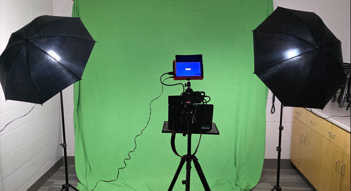 A green screen with studio lighting and a DSLR camera setup on a tripod. 